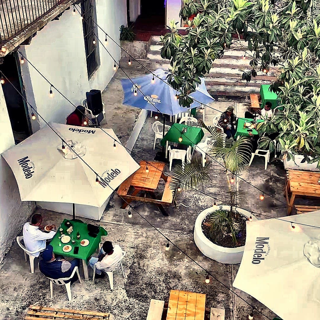 Vista aérea diurna del patio activo — árbol central, mesas, casona