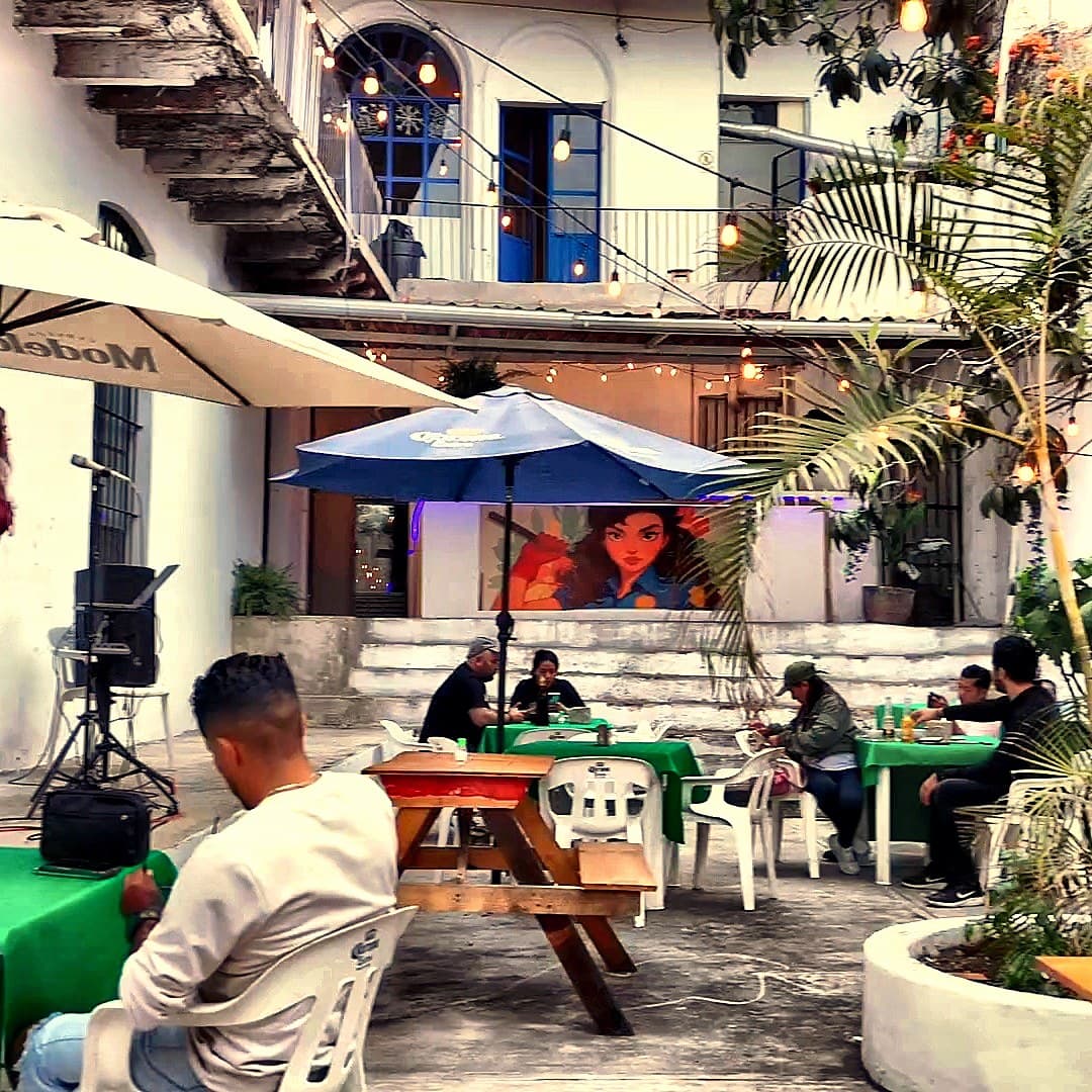 El patio de La Macana al crepúsculo — casona, árbol, string lights y gente en mesas